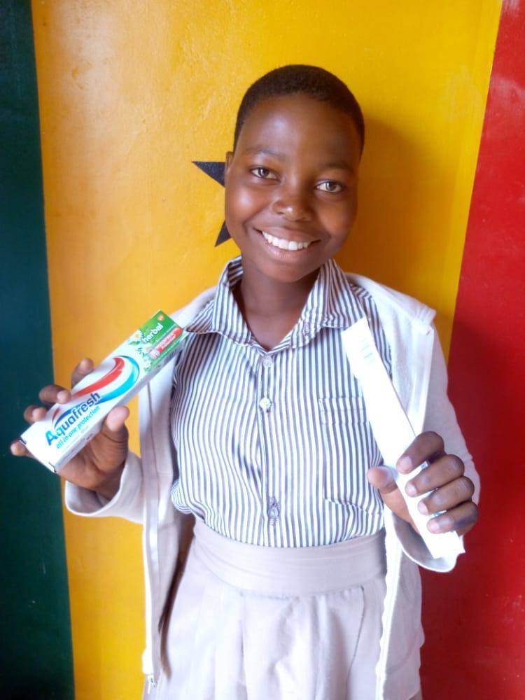 A girl happily shows her new toothbrush and tube of toothpaste