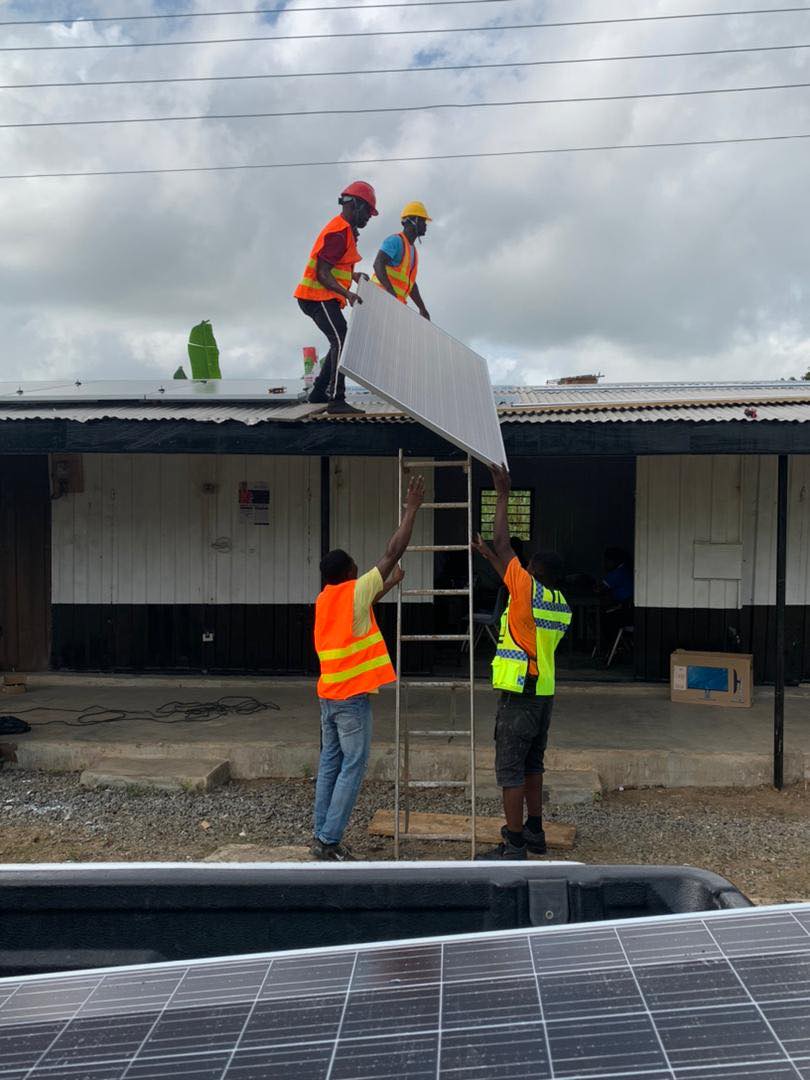 two men on ground hoist a solar panel up to two men on roof