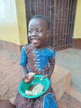 little girl smiles at camera as she pauses before taking another handful of food