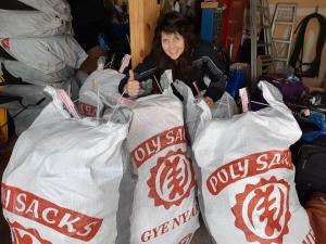 Carol stands behind four shipping bags full of shoes, thanks to friends in Aurora and Newmarket!