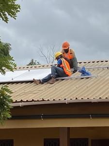 2 men are installing a solar panel on a roof of a building