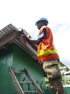 a man stand at the top of a ladder, installing a solar light to the corner of a toilet facility