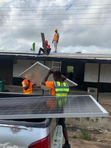 two mena taking a solar panel from a truck and lifting it to two men up on a roof
